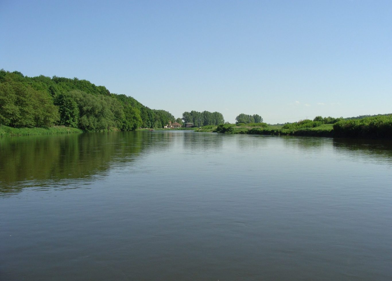 Ruhiger Fluss mit grünen Ufern unter klarem, blauem Himmel.