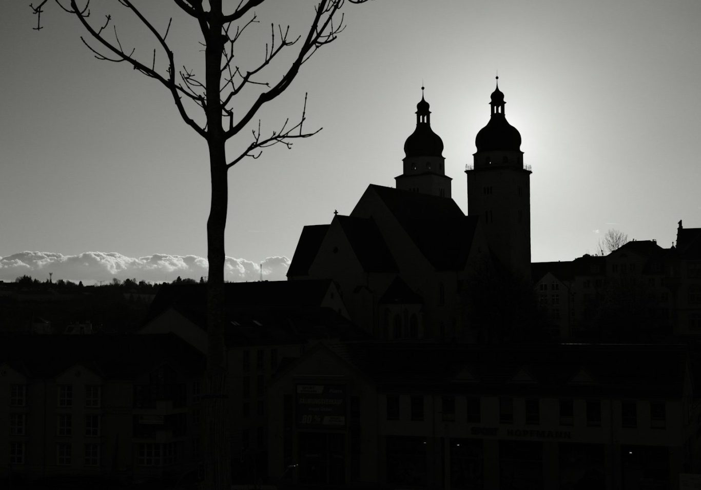 Dunkle Silhouette einer Kirche mit zwei Türmen vor einem hellen Himmel.