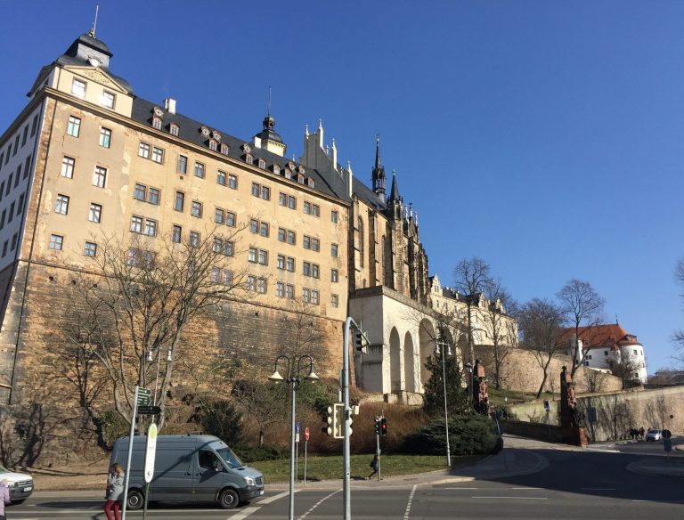 Historisches Gebäude mit neugotischem Stil, umgeben von Bäumen und klarem Himmel in Altenburg