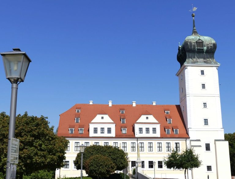 Historisches Gebäude in Delitzsch mit einem hohen Turm und roten Dach unter klarem Himmel.