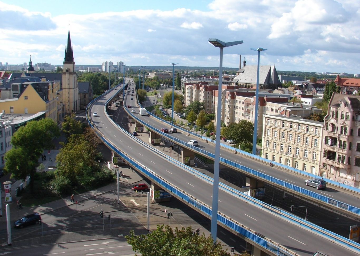 Stadtansicht mit einer Autobahn und der Skyline im Hintergrund, bewölkter Himmel.