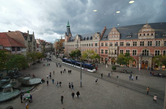 Anger in Erfurt mit historischem Gebäude, Straßenbahn und Menschenmenge bei bewölktem Himmel.