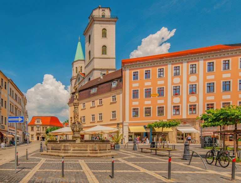 Blick auf einen Platz mit Brunnenin Zittau, historischen Gebäuden und blauen Himmel.