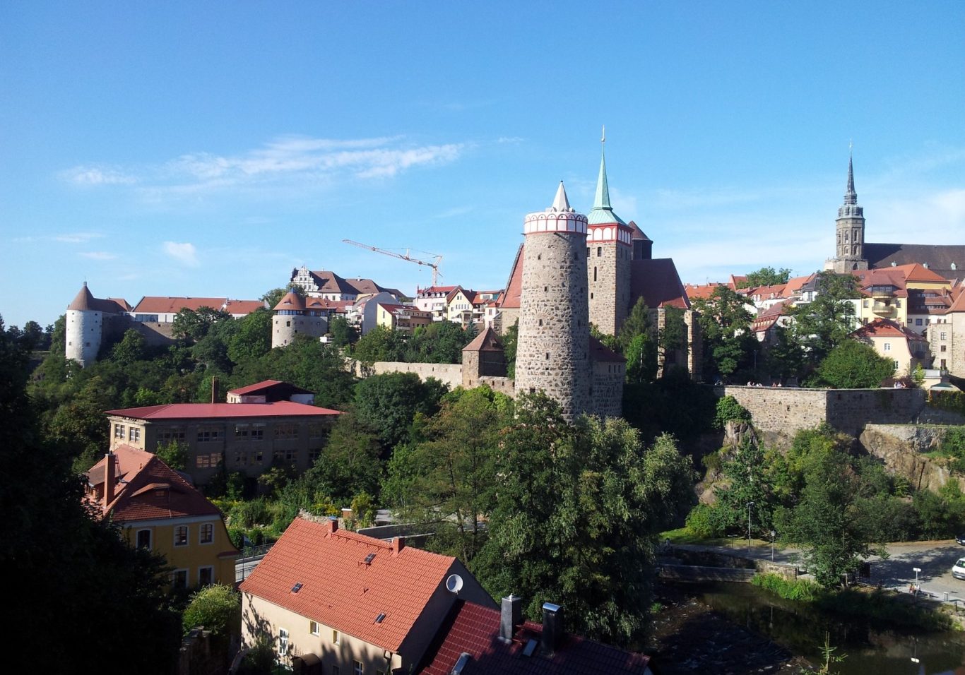 Blick auf eine historische Burganlage mit Türmen und grüner Umgebung.
