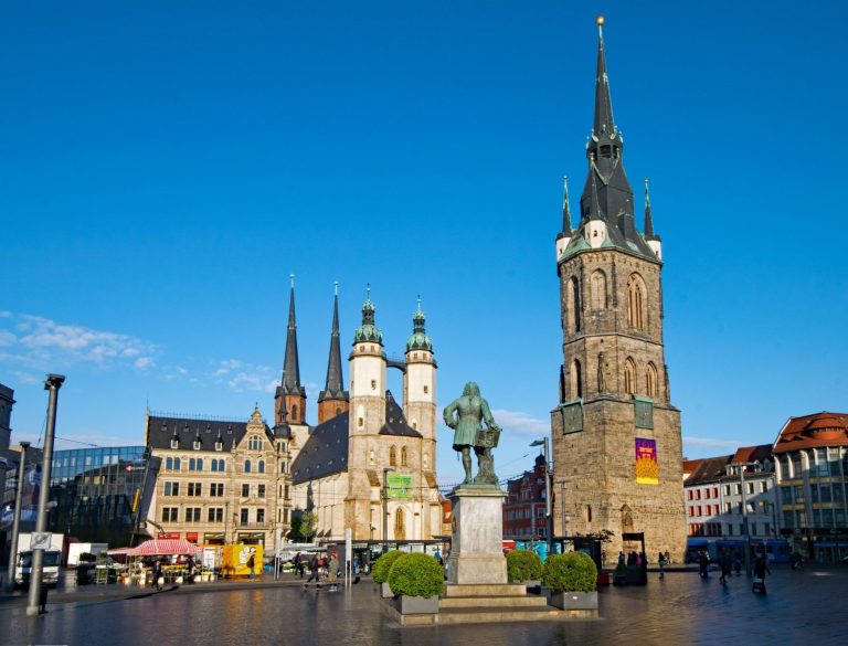 Marktplatz in Halle (Saale) mit historischem Gebäude, Uhrturm und Statue unter blauem Himmel.