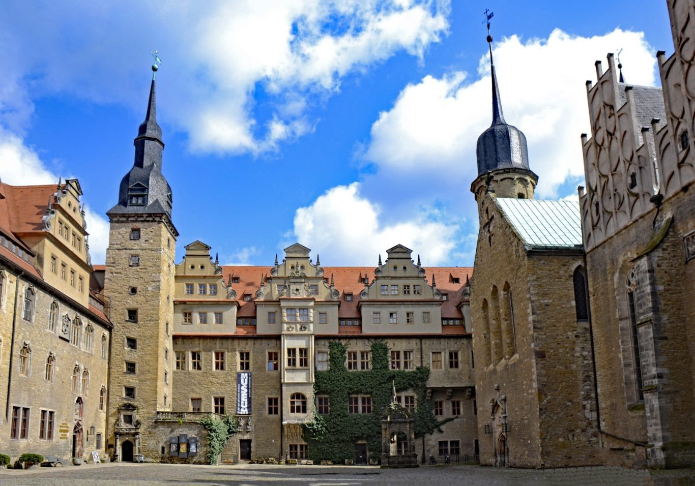 Blick auf einen historischen Schlossinnenhof mit Türmen und Wolken am Himmel.