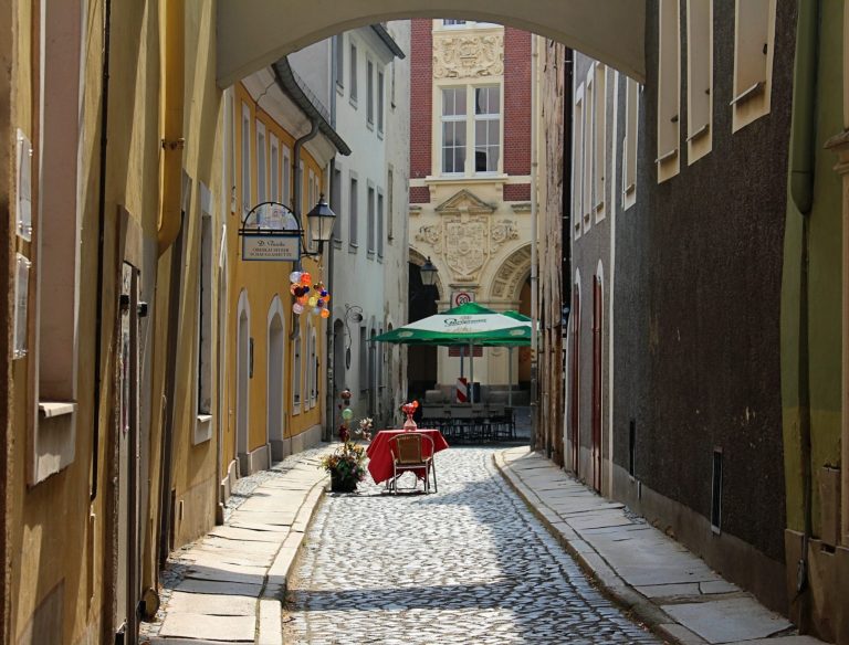 Enge Gasse in Görlitz mit cobblestone Boden und einem Tisch unter einem grünen Sonnenschirm.