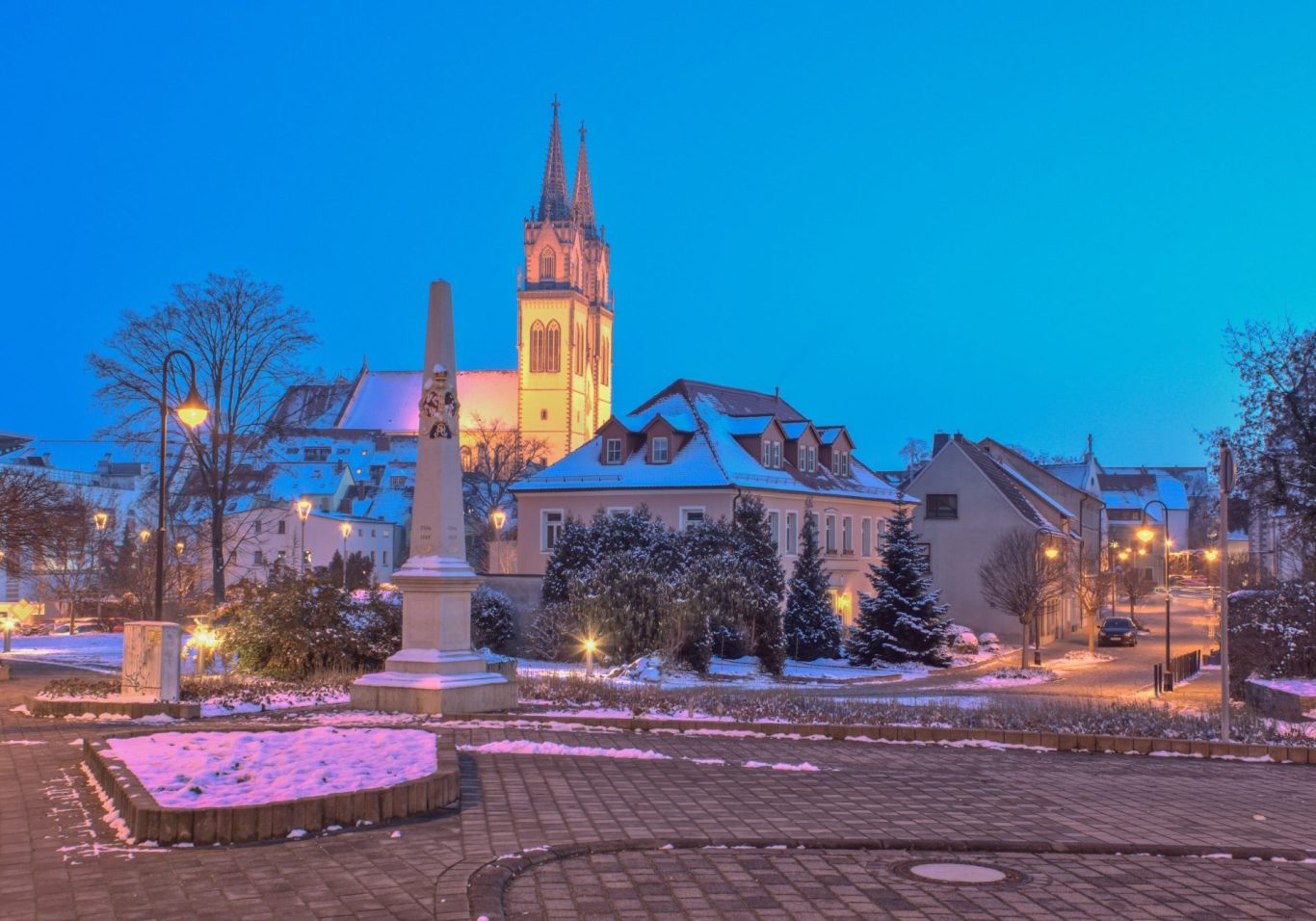 Winterliche Stadtansicht mit Kirche im Hintergrund und schneebedecktem Platz.