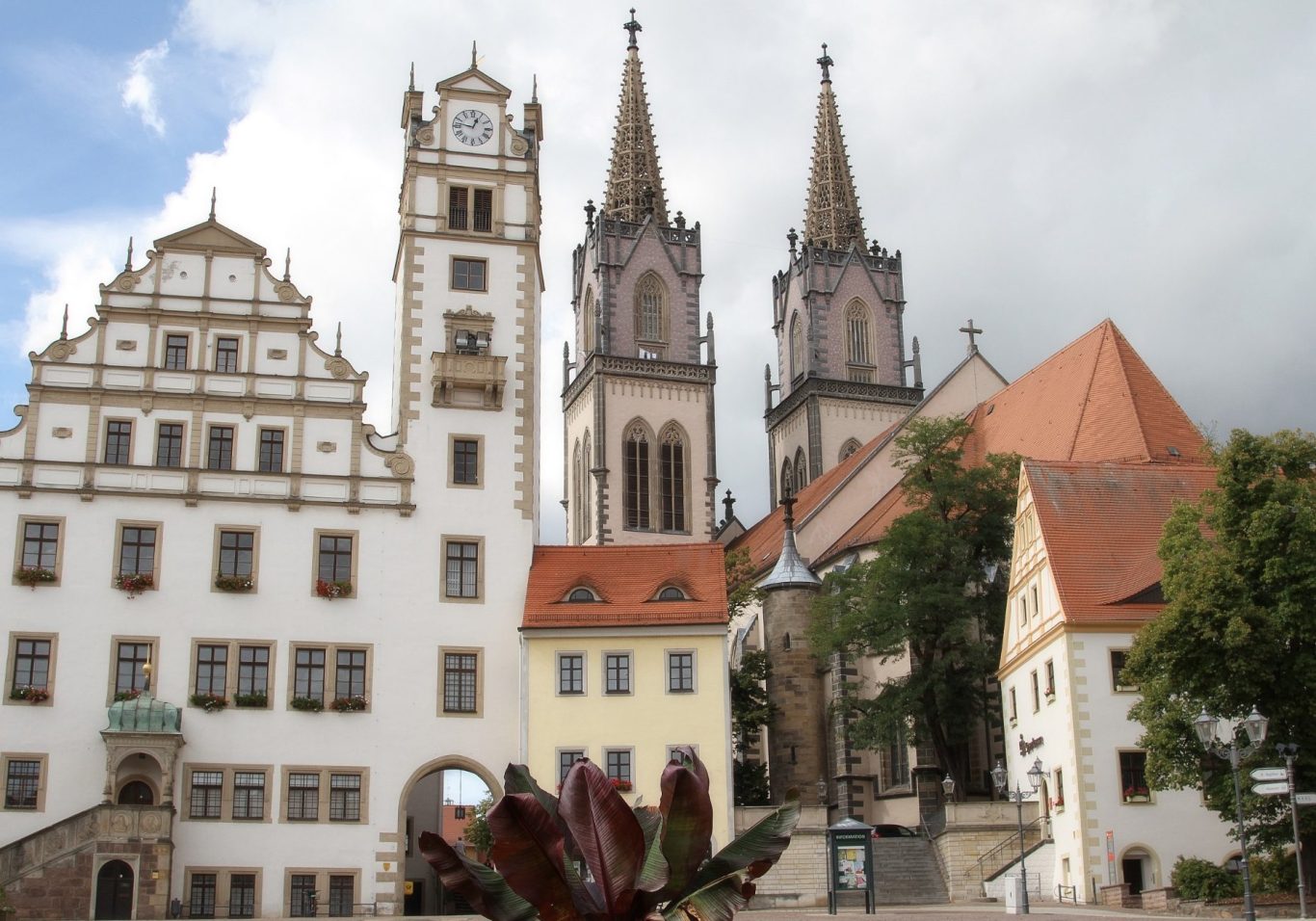 Historische Gebäude mit Türmen und einem Kirchturm im Vordergrund.