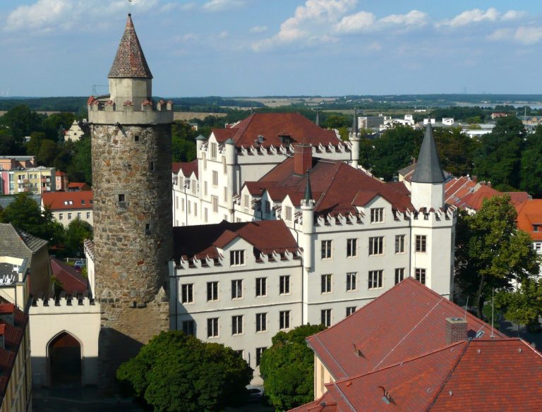 Historisches Gebäude in Bautzen mit Türmen und roten Dächern, umgeben von Bäumen.